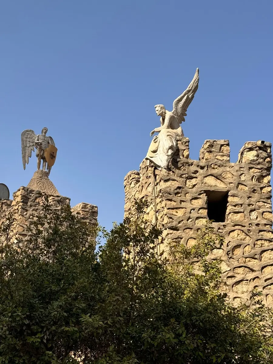 A ruined stone tower of the Babylon fortress with a statue on its top, trees below